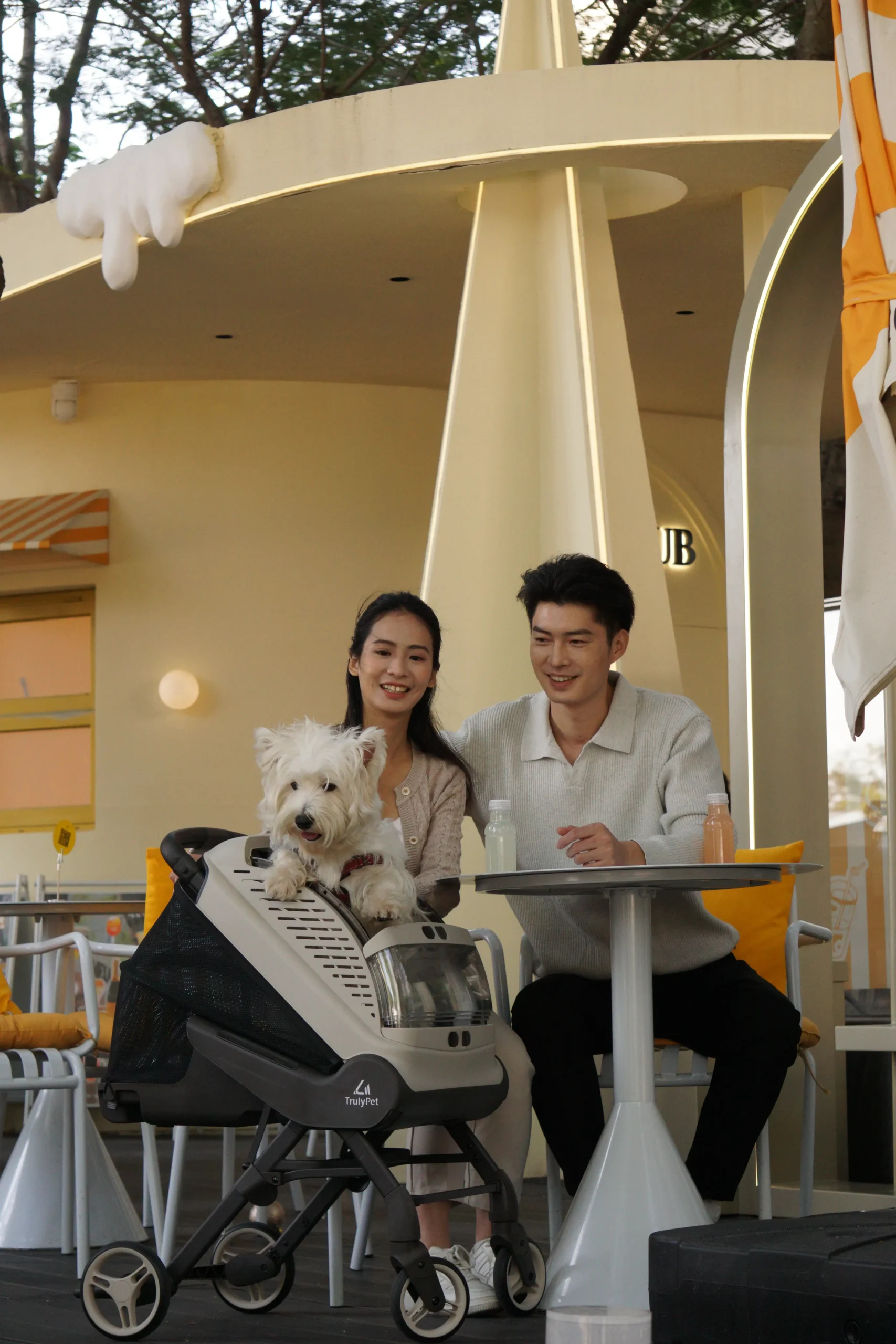 Couple at a cafe table with the TrulyPet Explorer pet stroller and their dog beside them