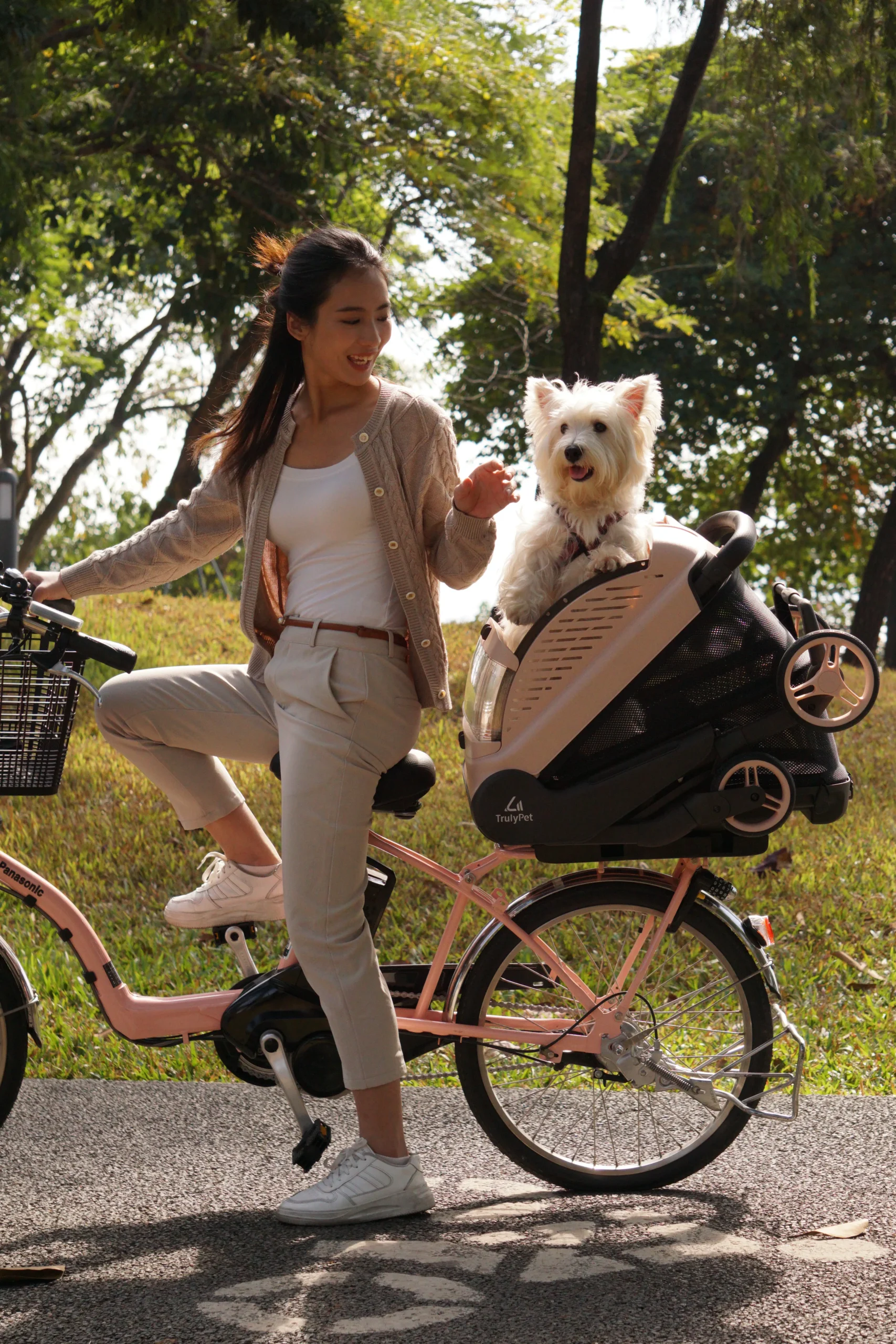Woman with her bicycle in a park, her white dog riding in the TrulyPet Explorer cabin in Bike mode