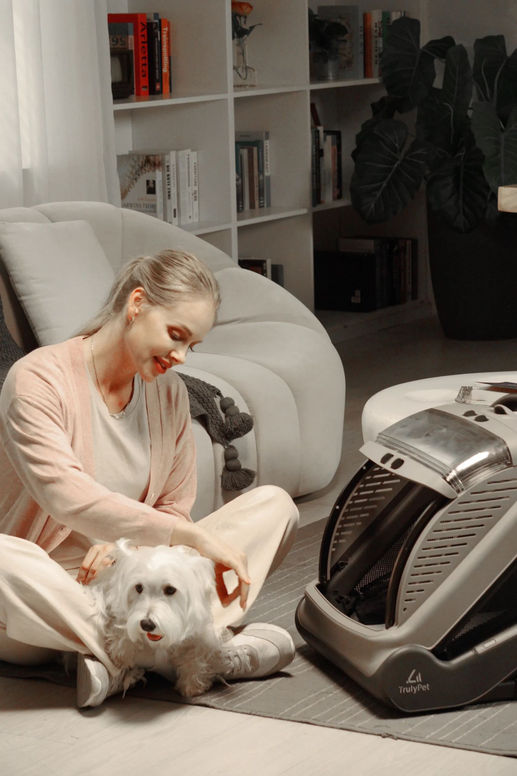 Woman sitting on the living room floor with her white dog beside the TrulyPet Explorer cabin in Nest mode
